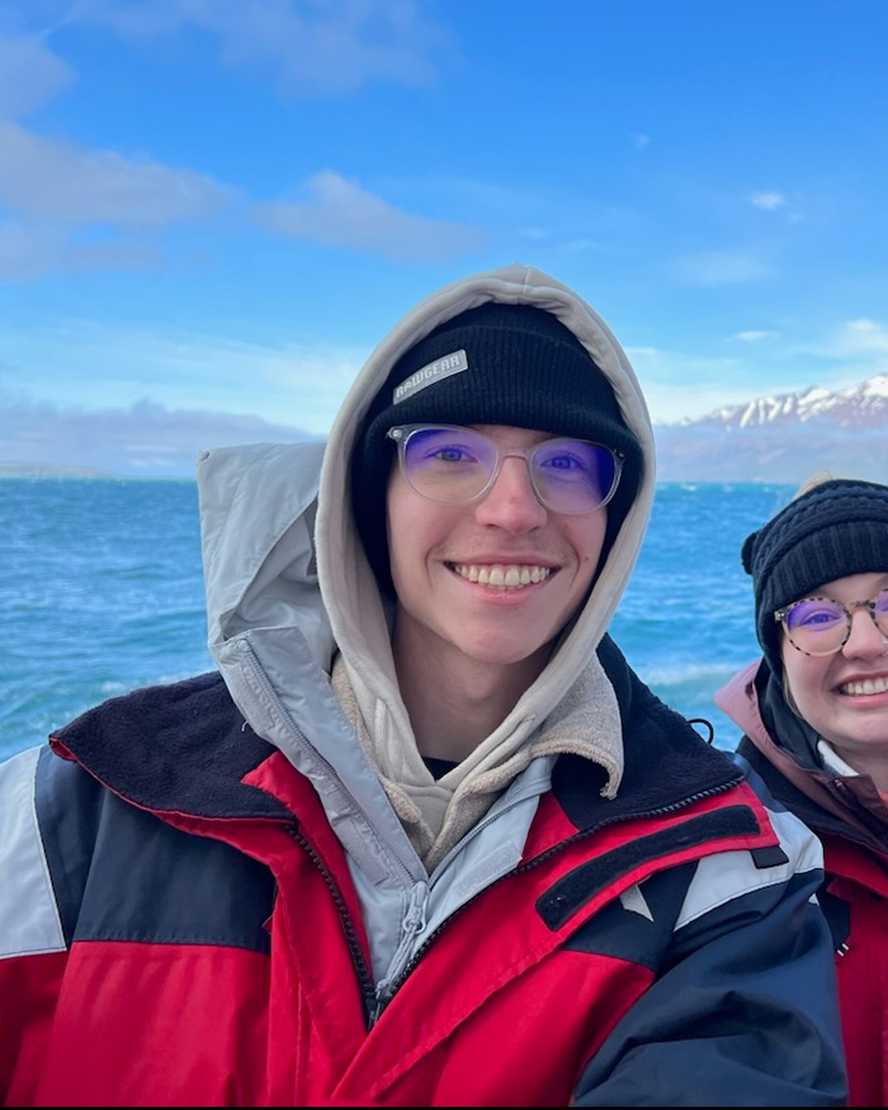 Ian Riley, smiling in a parka on a boat with a snow-capped coastline behind